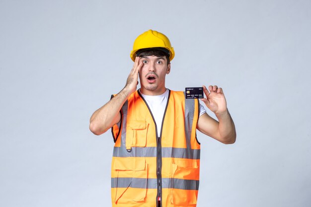 Vista frontal joven trabajador con tarjeta bancaria negra sobre fondo blanco.