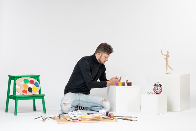 Vista frontal joven trabajando con pinturas en la pared blanca pintura arte color artista pintura foto imagen dibujar