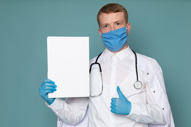 Una vista frontal joven en traje médico blanco guantes azules y máscara en el escritorio azul