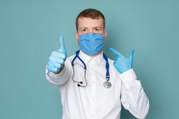 Una vista frontal joven en traje médico blanco guantes azules y máscara en el espacio azul