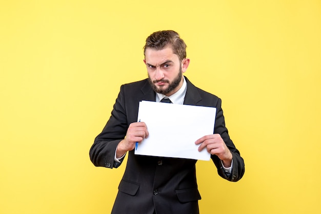 Vista frontal del joven en traje negro serio sosteniendo hojas de papel en blanco blanco con lugar para el texto en amarillo