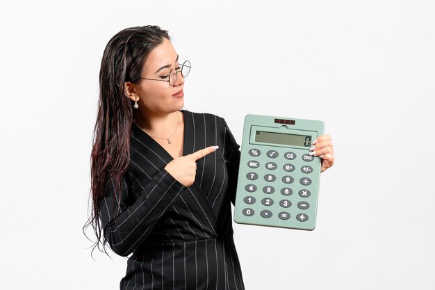 Vista frontal joven en traje oscuro estricto con gran calculadora sobre fondo blanco trabajo de oficina de negocios de moda de mujer de belleza