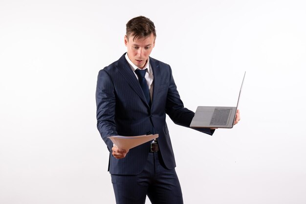 Vista frontal joven en traje usando su computadora portátil y comprobando archivos sobre fondo blanco.