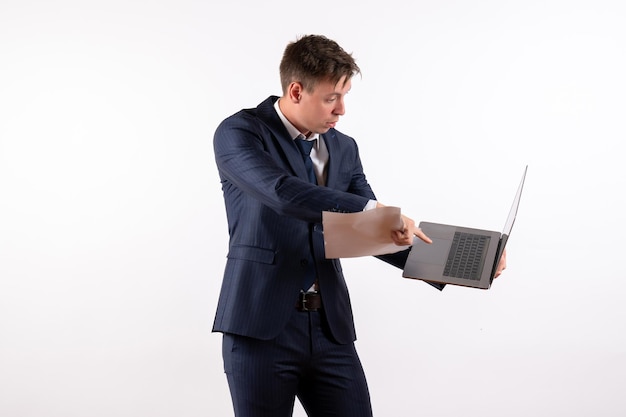 Vista frontal joven en traje usando su computadora portátil y comprobando archivos sobre fondo blanco.
