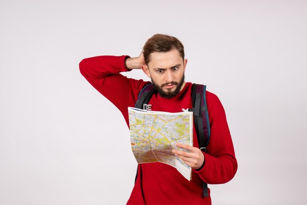 Vista frontal joven turista con mochila explorando el mapa en la pared blanca plano ciudad vacaciones emoción color humano turismo