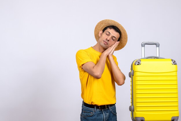 Vista frontal joven turista de pie junto a la maleta amarilla durmiendo