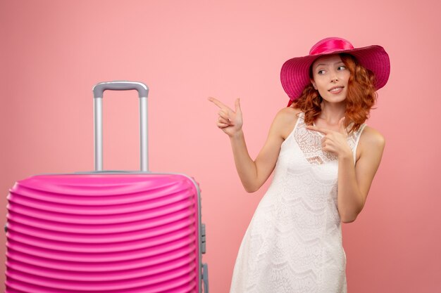 Vista frontal de la joven turista con sombrero rosa y bolso en pared rosa