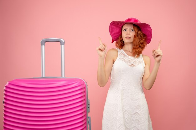Vista frontal de la joven turista con sombrero rosa y bolso en pared rosa