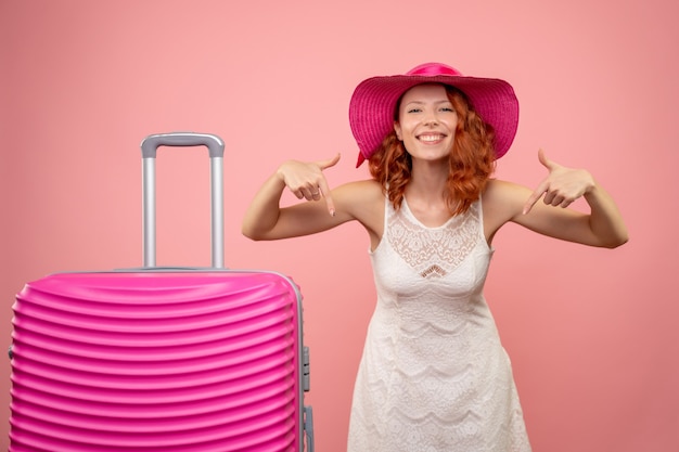 Vista frontal de la joven turista con sombrero rosa y bolso en pared rosa
