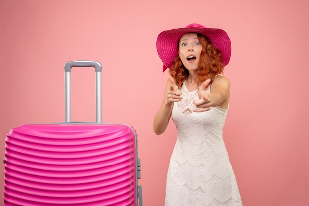 Vista frontal de la joven turista con sombrero rosa y bolso en pared rosa