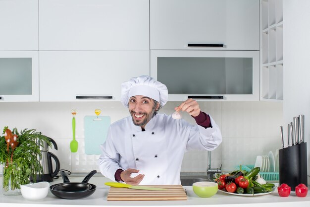 Vista frontal joven en uniforme sosteniendo ajo en la cocina