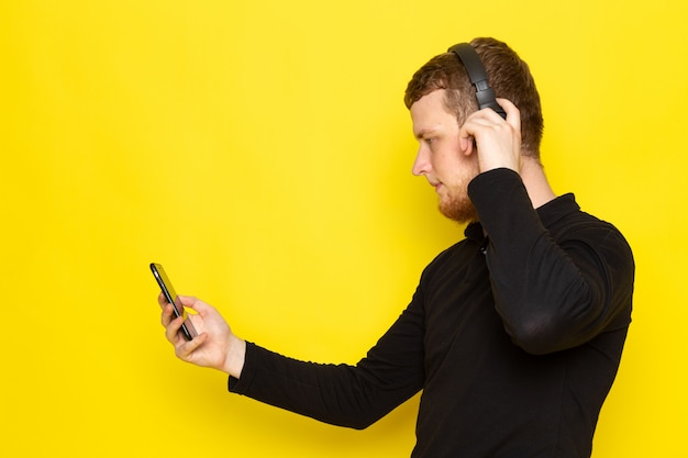 Vista frontal del joven varón en camisa negra escuchando música a través de auriculares