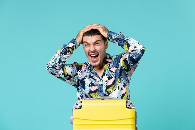 Vista frontal del joven varón preparándose para las vacaciones con bolsa gritando en la pared azul