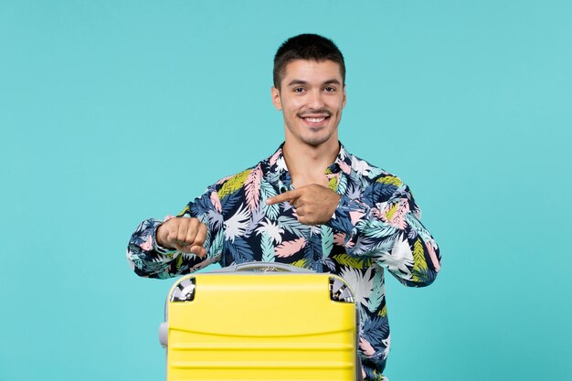 Vista frontal del joven varón preparándose para las vacaciones con su bolsa amarilla en la pared azul