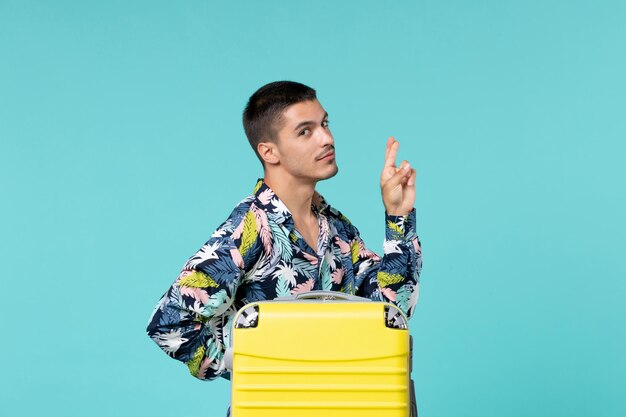 Vista frontal del joven varón preparándose para el viaje con su bolsa amarilla sobre superficie azul