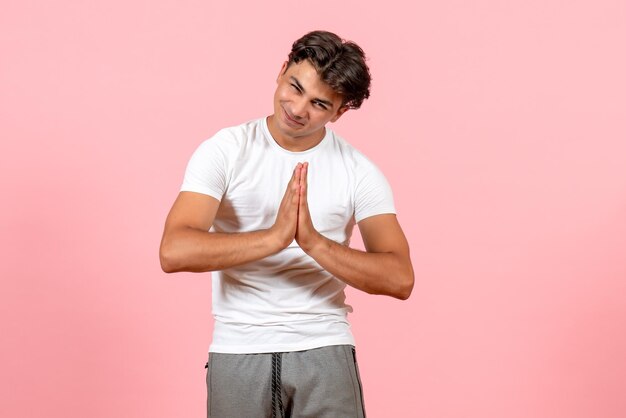 Vista frontal joven varón rezando en camiseta blanca sobre fondo rosa