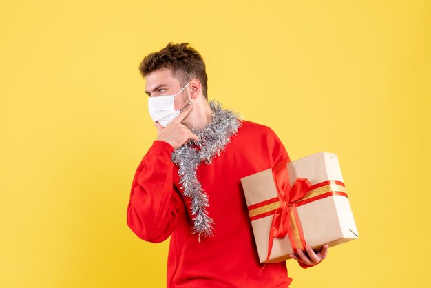 Vista frontal joven varón sosteniendo Navidad presente en máscara estéril