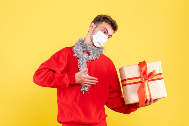 Vista frontal joven varón sosteniendo el regalo de Navidad en máscara estéril