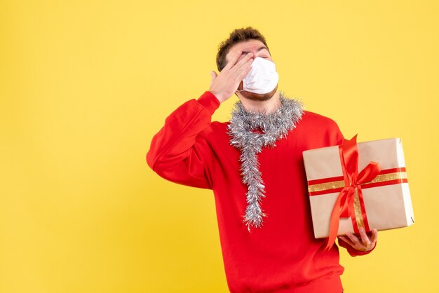 Vista frontal joven varón sosteniendo regalo de Navidad en máscara