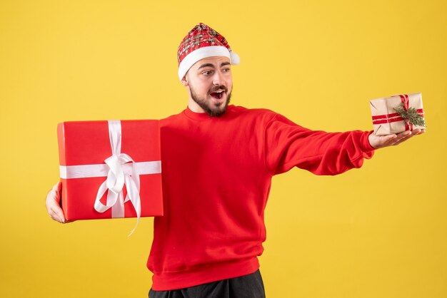 Vista frontal joven varón sosteniendo regalos de Navidad sobre fondo amarillo