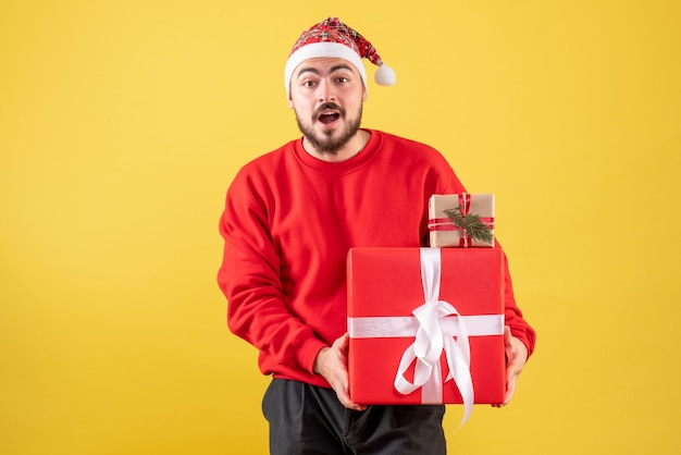 Vista frontal joven varón sosteniendo regalos de Navidad sobre fondo amarillo