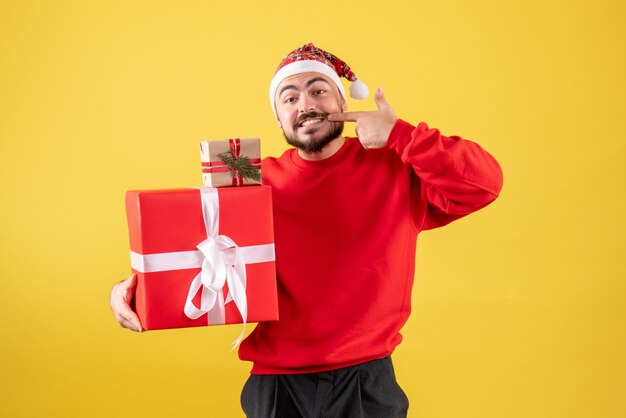 Vista frontal joven varón sosteniendo regalos de Navidad sobre fondo amarillo
