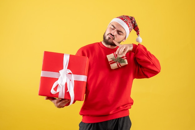 Vista frontal joven varón sosteniendo regalos de Navidad sobre fondo amarillo