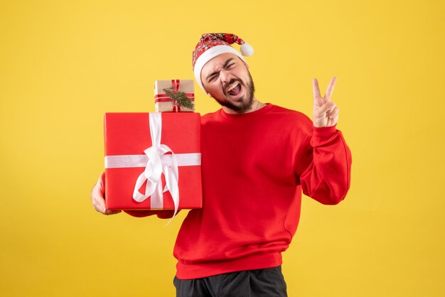 Vista frontal joven varón sosteniendo regalos de Navidad sobre fondo amarillo