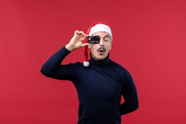 Vista frontal joven varón sosteniendo una tarjeta bancaria negra en el piso rojo vacaciones emoción de año nuevo