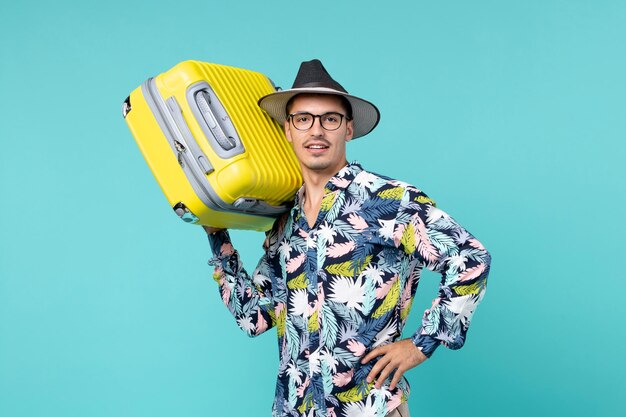Vista frontal del joven varón de vacaciones y sosteniendo su bolsa amarilla en el espacio azul