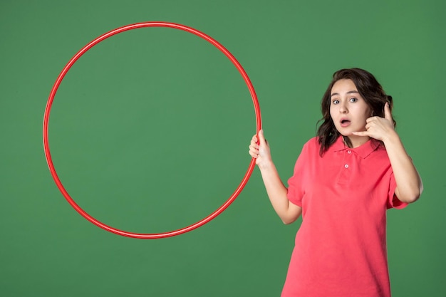 Vista frontal joven vendedora sosteniendo hula hoop rojo sobre un fondo verde cuerpo de yoga uniforme trabajo atleta trabajo dinero compras venta