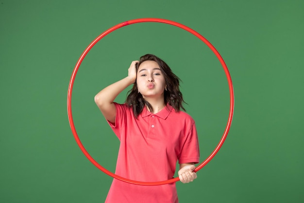 Vista frontal joven vendedora sosteniendo hula hoop rojo sobre fondo verde cuerpo de yoga venta uniforme comercial atleta trabajo deporte