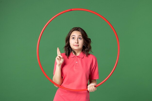 Vista frontal joven vendedora sosteniendo hula hoop rojo sobre fondo verde yoga cuerpo venta uniforme trabajo compras atleta deporte