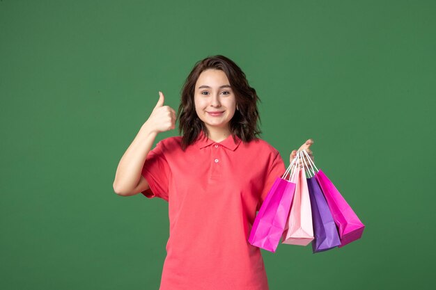 Vista frontal joven vendedora sosteniendo pequeños paquetes sobre fondo verde trabajo color trabajador boutique venta presente compras