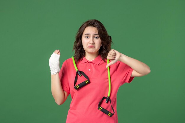 Vista frontal joven vendedora con vendaje en su mano herida sobre fondo verde color lesión salud hospital compras trabajo uniforme