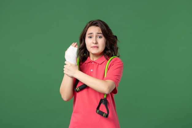 Vista frontal joven vendedora con vendaje en su mano herida sobre fondo verde trabajo color lesión salud hospital compras uniforme