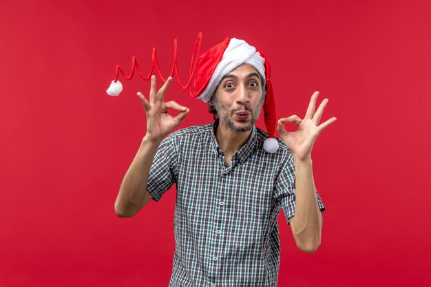 Vista frontal del joven vestido con gorro de juguete de navidad en la pared roja