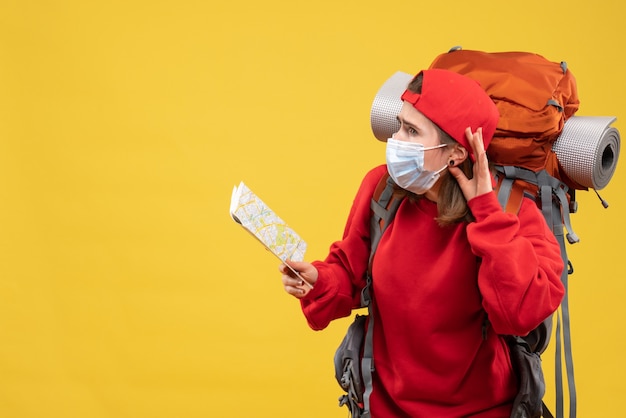 Foto gratuita vista frontal joven viajera con mochila y máscara con mapa escuchando algo