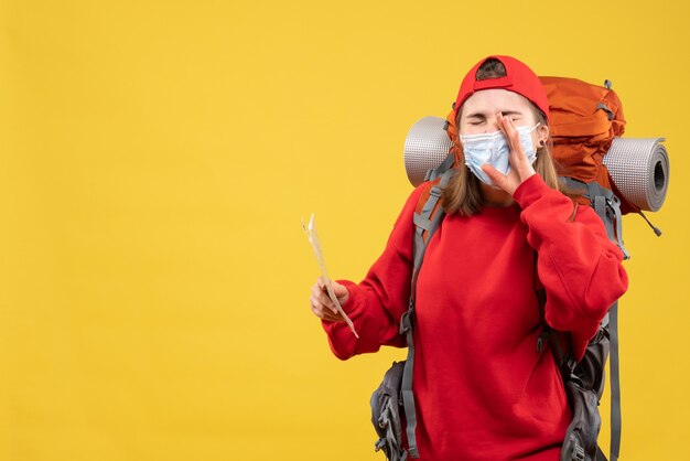 Vista frontal joven viajera con mochila y máscara con mapa llamando a alguien