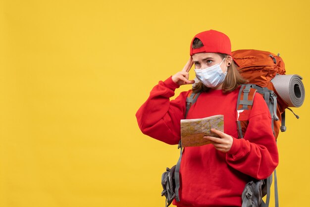 Vista frontal joven viajera con mochila y máscara con mapa pensando