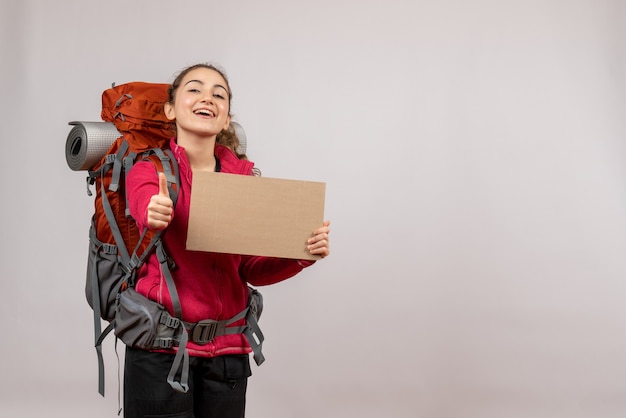 Foto gratuita vista frontal joven viajero con mochila grande sosteniendo cartón dando pulgar hacia arriba