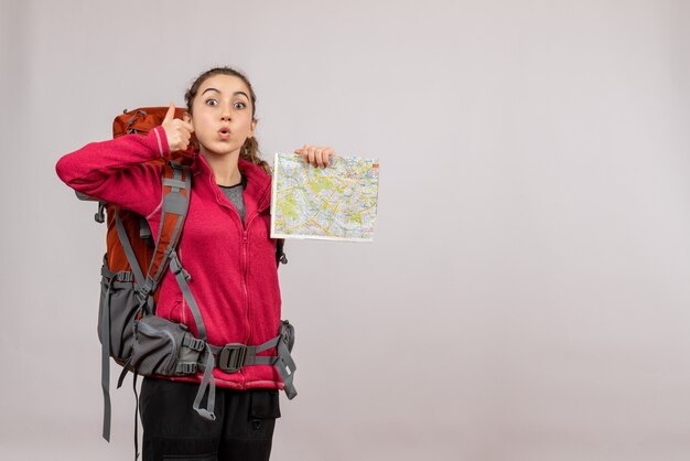 Vista frontal joven viajero con mochila grande sosteniendo haciendo pulgares arriba mapa de señal