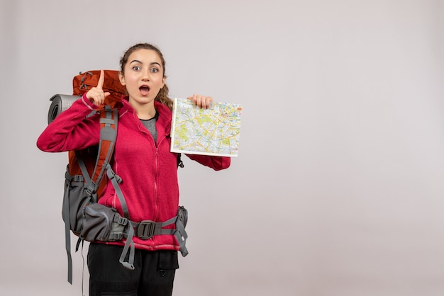 Vista frontal joven viajero con mochila grande sosteniendo el mapa apuntando con el dedo hacia arriba