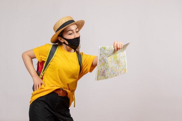 Vista frontal joven viajero con mochila mirando el mapa poniendo la mano en la cintura