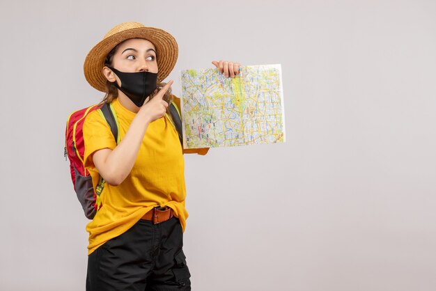 Vista frontal joven viajero con mochila sosteniendo el mapa apuntando con el dedo hacia arriba