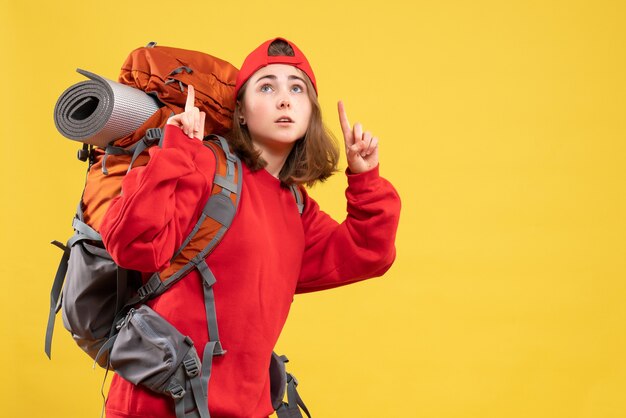 Vista frontal joven viajero mujer en mochila roja apuntando con el dedo hacia arriba
