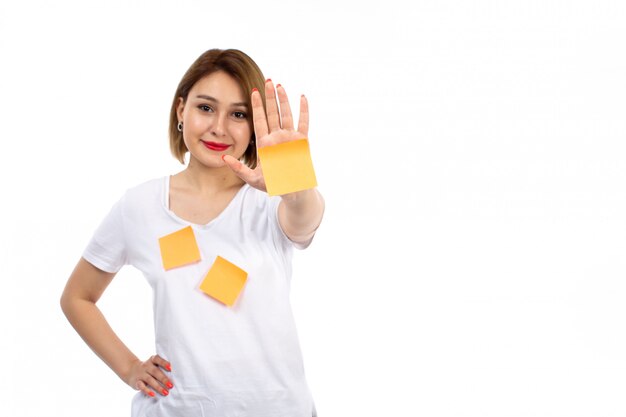 Una vista frontal jovencita en camisa blanca con notas naranjas posando sonriendo en el blanco