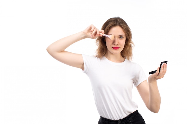 Una vista frontal jovencita en camisa blanca y pantalón negro haciendo maquillaje en el blanco