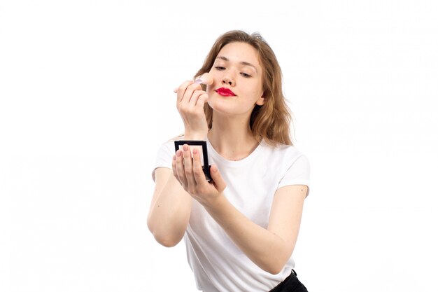 Una vista frontal jovencita en camisa blanca y pantalón negro haciendo maquillaje en el blanco