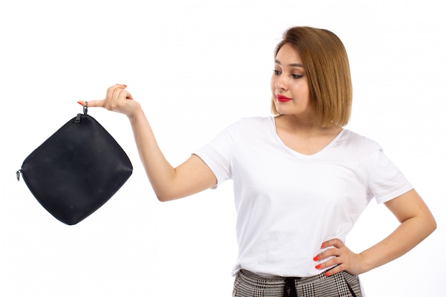 Una vista frontal jovencita con camisa blanca y pantalones modernos ligeros con bolso negro sobre el blanco